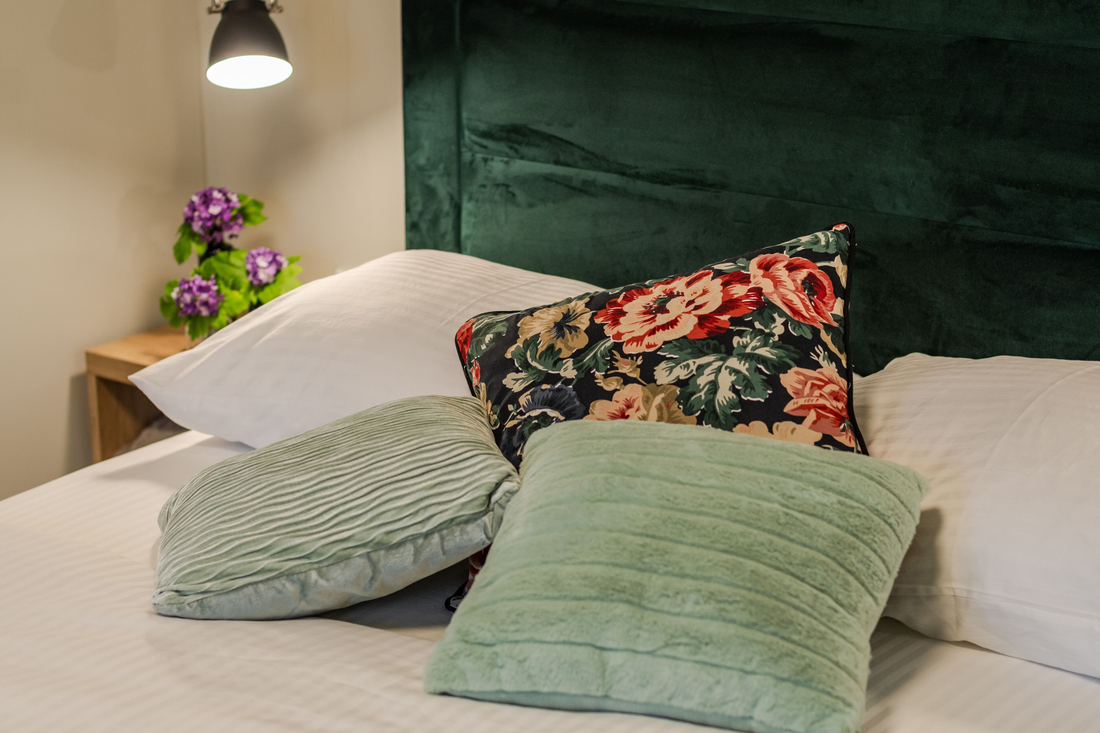 A neatly made bed with green and white pillows, a floral pillow, and a green headboard.