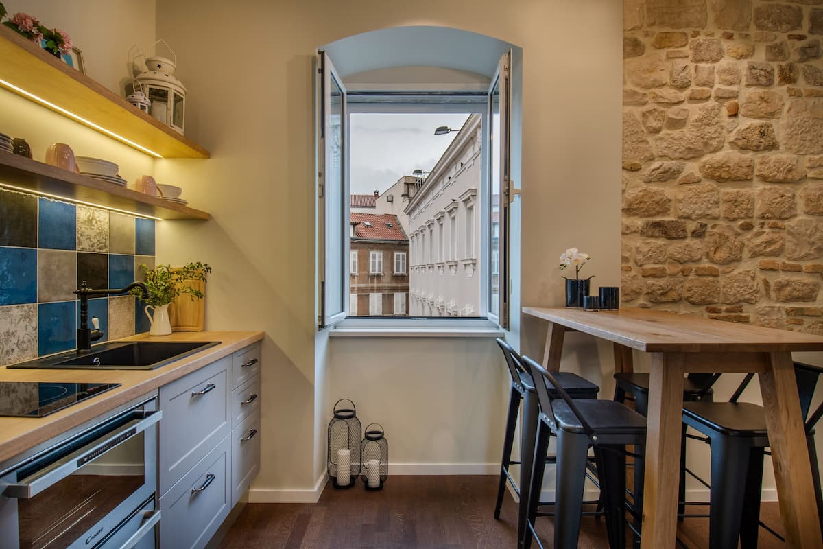 A compact kitchen with a window view, built-in appliances, and a stone wall.