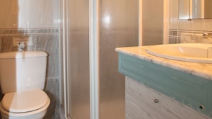 Baño con cabina de ducha, inodoro y tocador con lavabo.