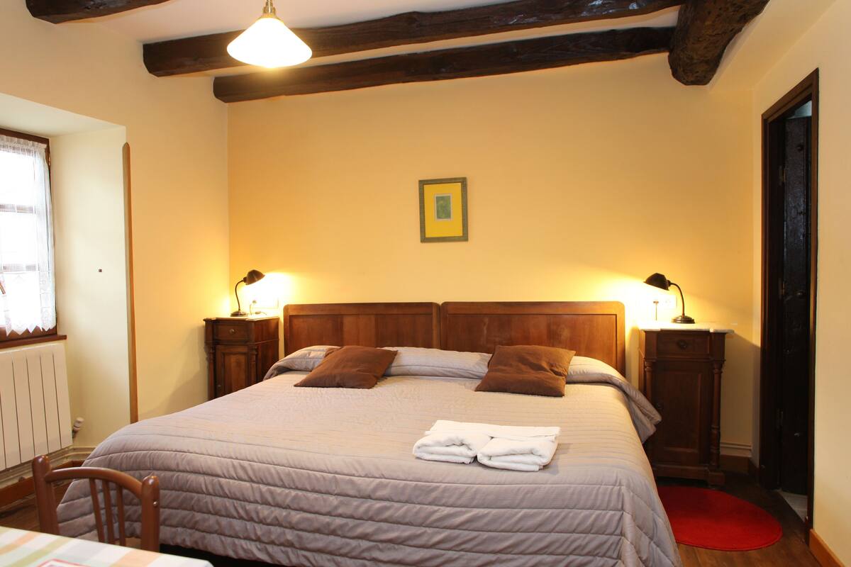 A neatly made bed with a headboard, two bedside tables with lamps, a small framed picture on the wall, and a red rug on the floor.