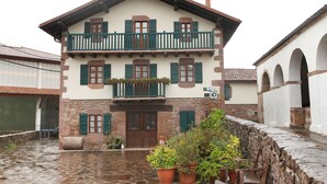 Un edificio tradicional con fachada de piedra, contraventanas de madera y un balcón con barandilla verde.