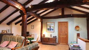 Una habitación acogedora con techo de madera, un sofá verde a cuadros, un aparador de madera y una mesa con libros.