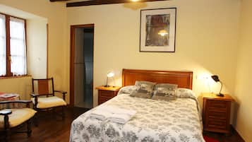 A bedroom with a large bed, two bedside tables with lamps, a chair, and a door leading to another room.