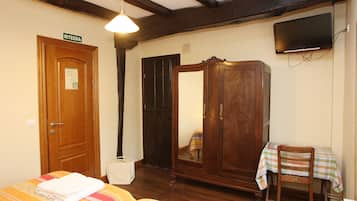 Una habitación con una cama, un armario de madera, una mesa con mantel a cuadros, un televisor montado en la pared y una puerta con la leyenda "IRTEERA".