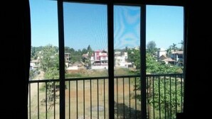 A view from a window with a metal railing, overlooking a residential area with houses and greenery. - Dean Villa (Mawal)