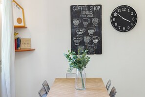 Un área de comedor con una mesa de madera, sillas, un letrero de cafetería, un reloj y un cuadro en la pared.