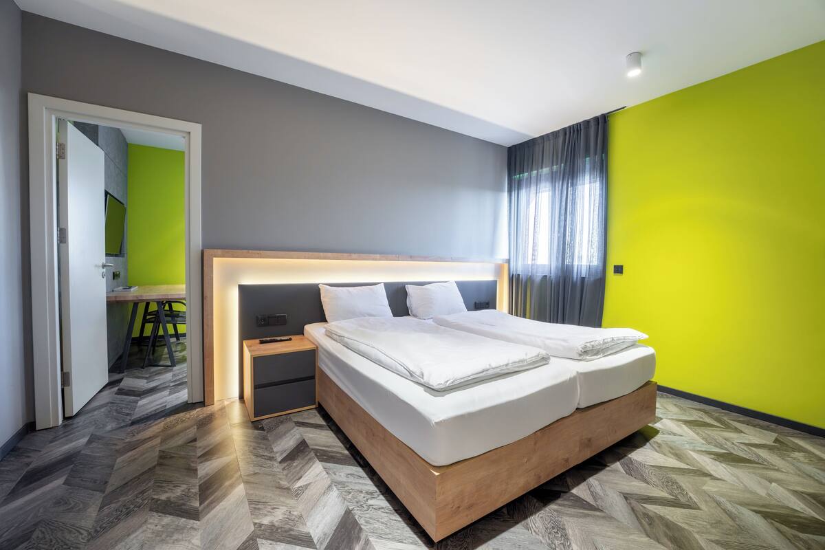 A modern hotel room with a large bed, a bedside table, and a view of a dining area.