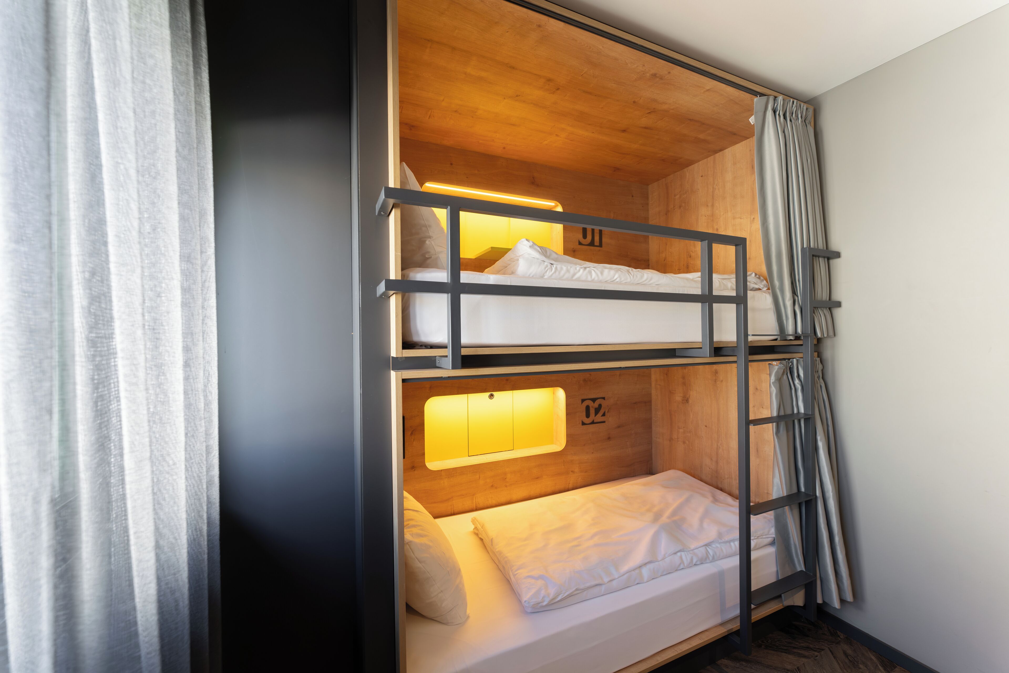 Camera con letto a castello, una testiera in legno, una scala e una piccola finestra con una luce.