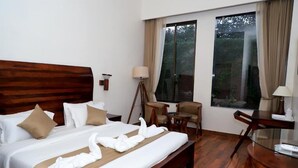 A hotel room with a large bed, a desk, a chair, and a window with curtains. - Aroma Resort Pushkar (Pushkar)