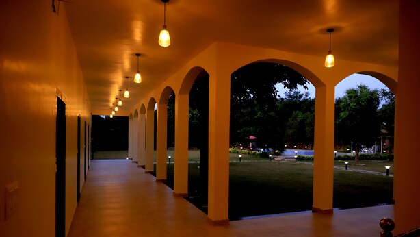 A corridor with arched ceilings and hanging lights, leading to an outdoor area with a lawn and trees. - Aroma Resort Pushkar (Pushkar)