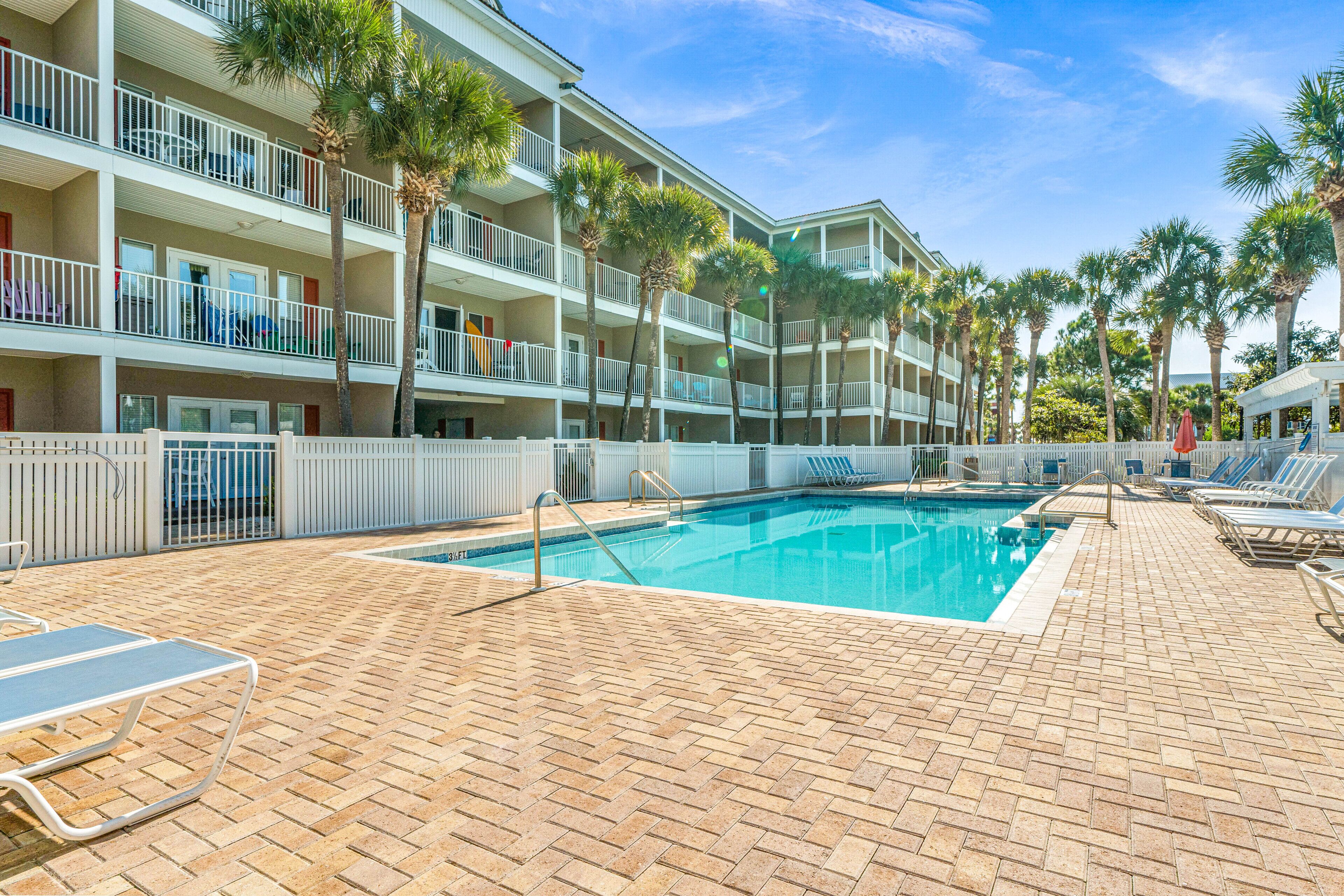 A hotel pool area with a brick deck, lounge chairs, and palm trees.