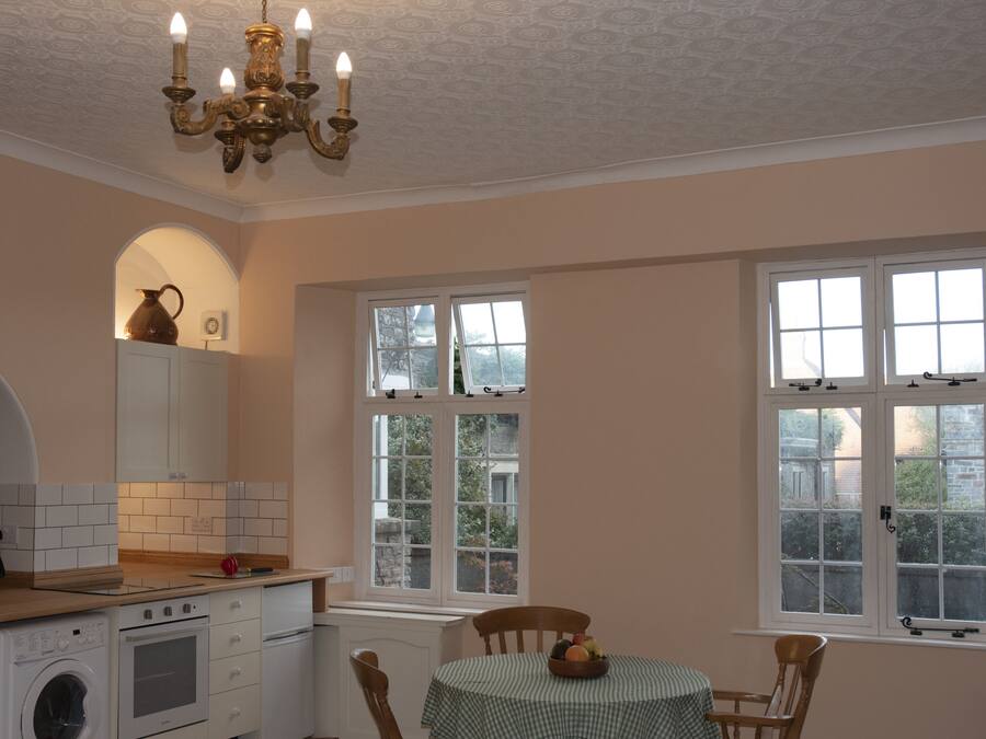 A kitchen with a washing machine, oven, and a chandelier. There are two windows and a table with chairs.
