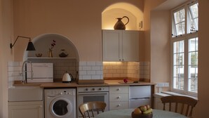 A compact kitchen with a washing machine, oven, and a table with fruit. - The Orangery Apartment (Bristol)