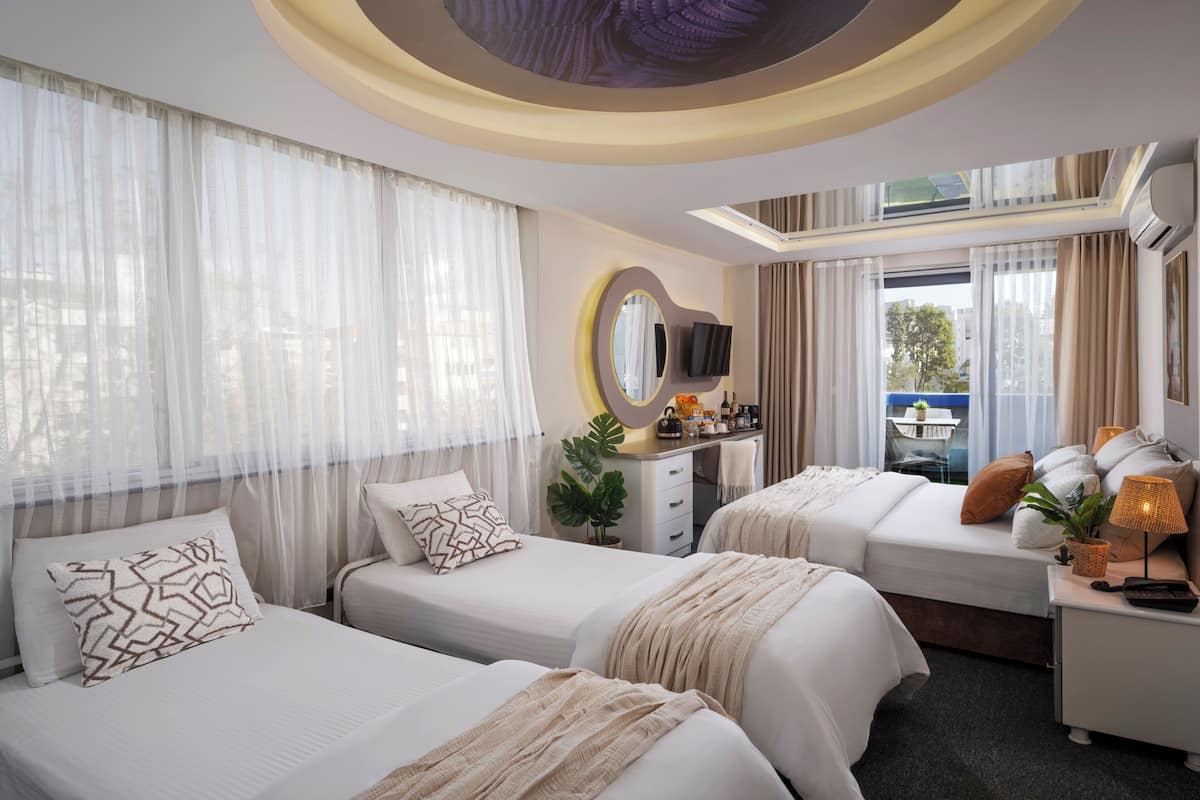 A hotel room with two beds, a desk, a TV, and a large window with curtains.