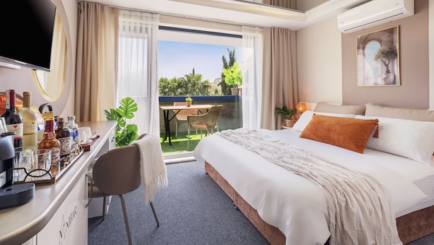 A hotel room with a bed, a desk with a computer, a TV, and a balcony with plants. - IS Hotel (Antalya)