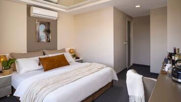 A modern hotel room with a large bed, bedside tables, a desk, and a minibar.
