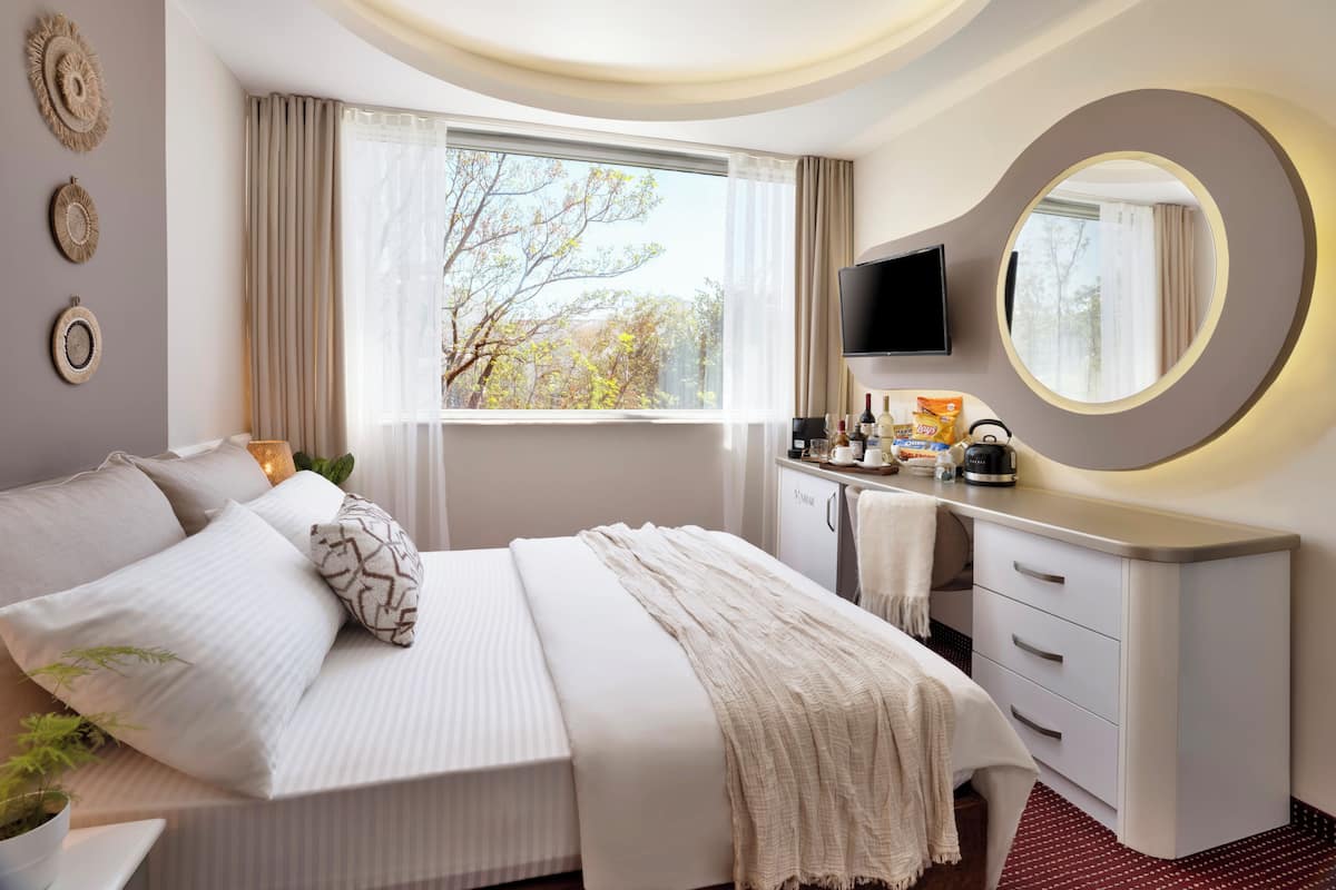 A modern hotel room with a bed, bedside table, TV, and a large window with curtains.