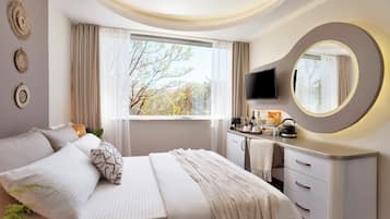 Una habitación de hotel moderna con cama, mesita de noche, televisor y un amplio ventanal con cortinas.