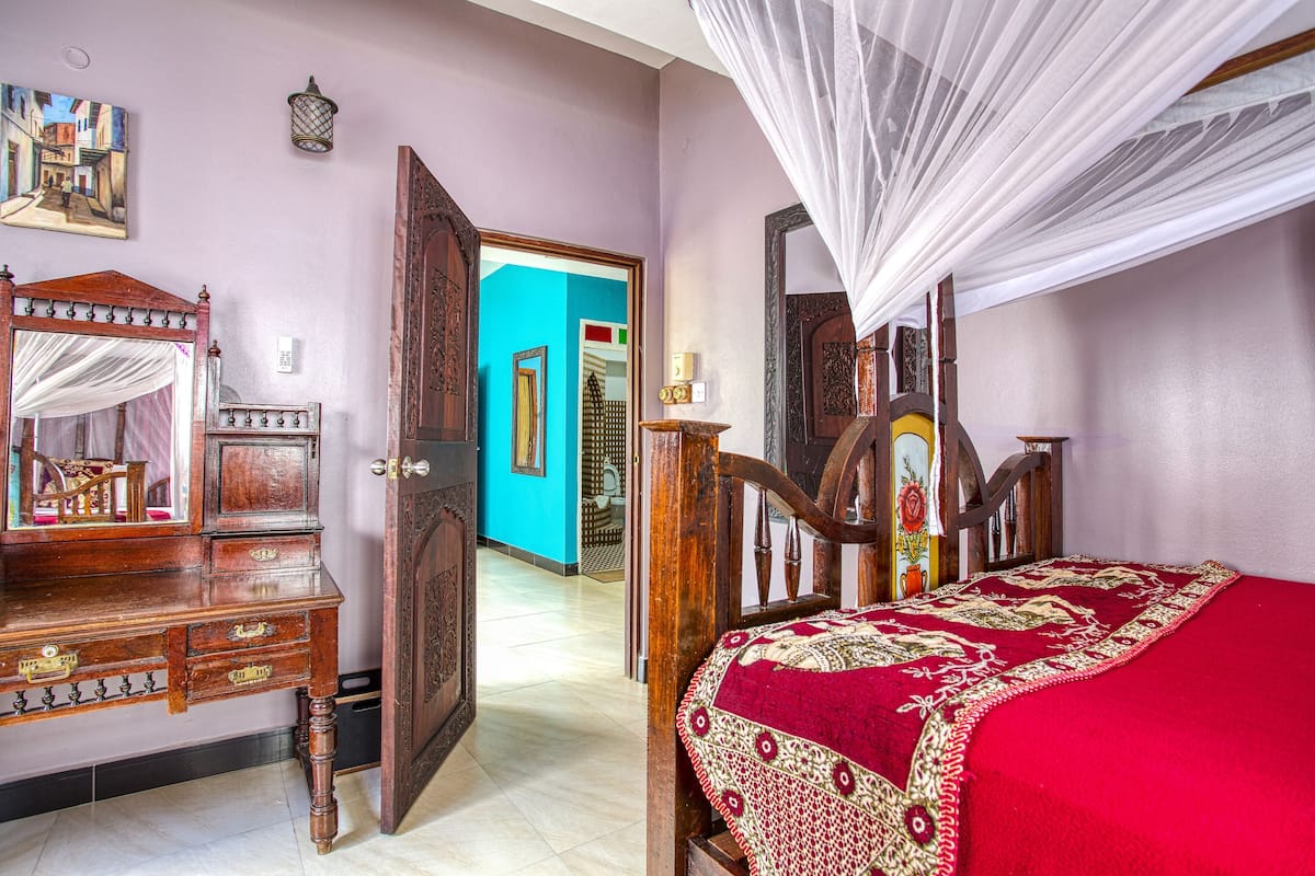A bedroom with a bed, a wooden dresser, a mirror, and a door leading to another room.