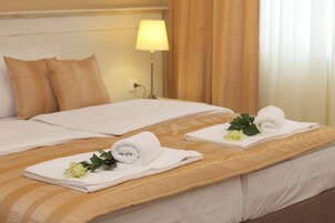Habitación de hotel con dos camas, cada una con una toalla blanca enrollada y una rosa amarilla.