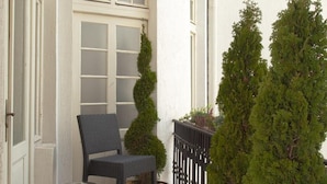 A small outdoor balcony with a chair, a trash can, and potted plants. - Booking Rooms (Belgrade)
