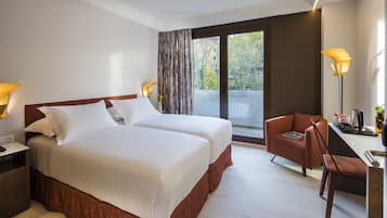 Habitación de hotel con dos camas, un escritorio con silla, una lámpara y vistas al exterior.