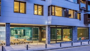 Un hotel moderno con fachada de vidrio, zona de estar al aire libre y entrada visible.