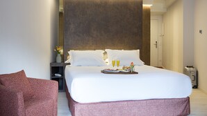 Habitación de hotel moderna con una cama grande, una mesita de noche con un jarrón de flores y una bandeja con artículos para el desayuno.