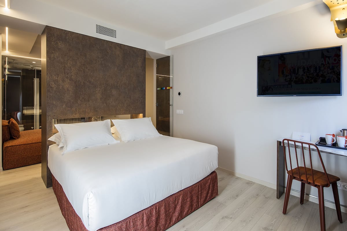 A modern hotel room with a large bed, a desk with a chair, and a television on the wall.