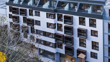 Un hotel moderno con terraza en la azotea, varios balcones y una chimenea de ladrillo.