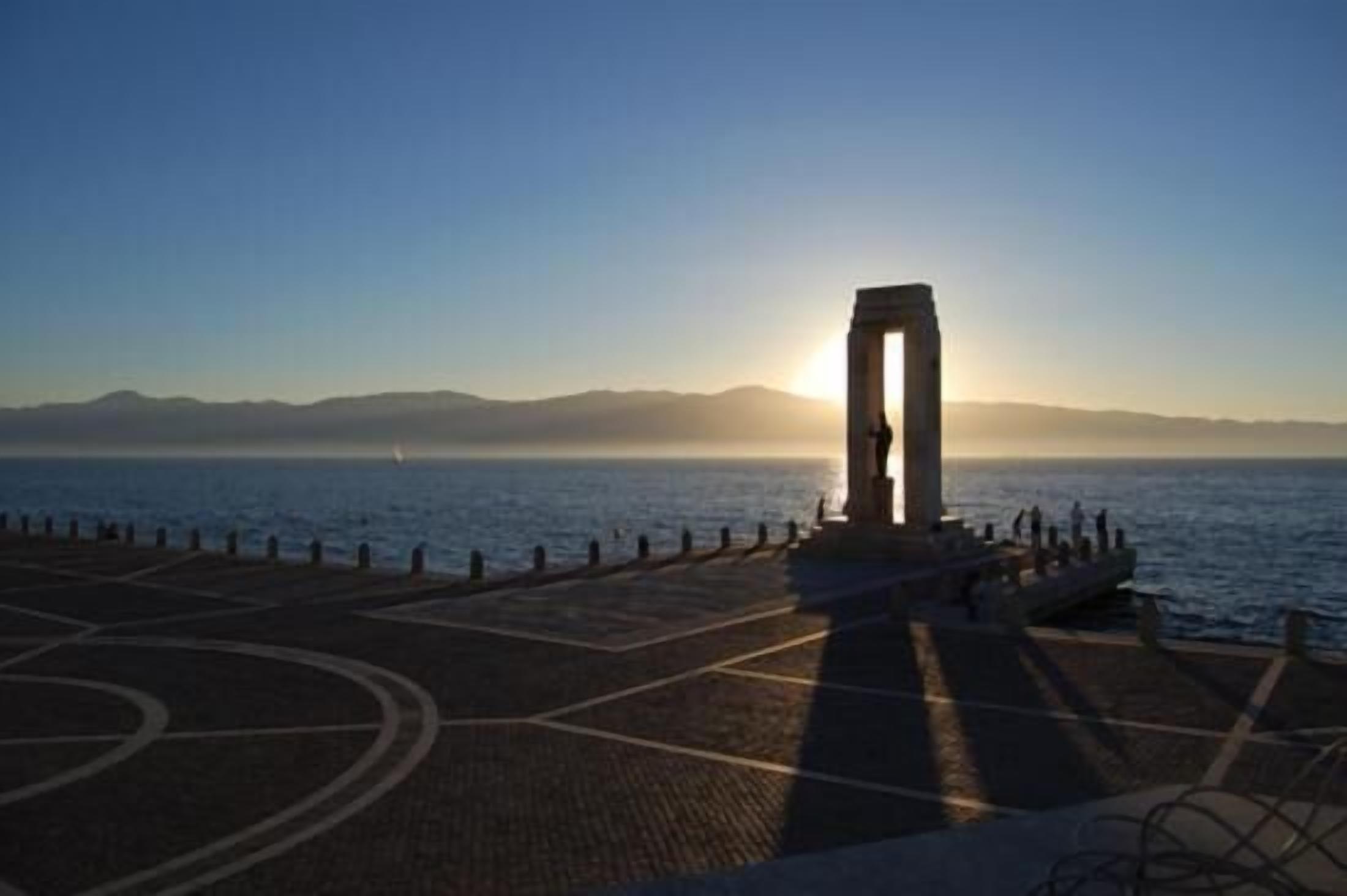 A coastal area with a stone monument and a paved walkway leading to the sea.