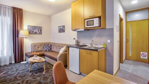 Habitación de hotel compacta con kitchenette, sofá, pequeña mesa de comedor y una silla.