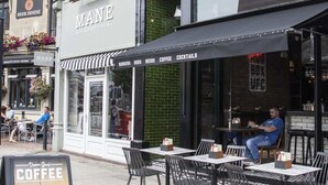 A street view of a cafe with outdoor seating, a sign for 'MANE HAIRDRESSING', and a 'HUBBOX' sign above the entrance. - Higgihaus at Hampton Whole House 6 Bed (Bristol)