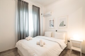 A modern hotel room with a large bed, white bedding, a bedside table with a lamp, and two framed pictures on the wall. - Urban Serenity Gem in Kallithea Area (Kallithea)