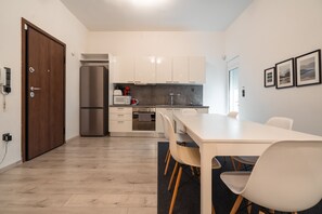 A modern kitchen with white cabinets, a stainless steel refrigerator, and a dining area with a white table and chairs. - Urban Serenity Gem in Kallithea Area (Kallithea)