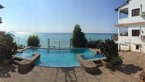 A pool area with a view of the sea, surrounded by buildings. - Rezz Aparthotel (Pemba)