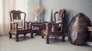 A room with two ornate wooden chairs, a small table with a vase, and a decorative shield-like object. - Rezz Aparthotel (Pemba)