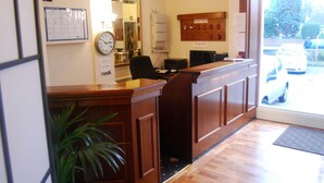 Un espace d’accueil avec un bureau en bois, une horloge, un miroir et un tableau d’affichage.
