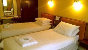 Une chambre d’hôtel avec deux lits simples, chacun agrémenté d’une serviette soigneusement pliée et d’une tête de lit. On y trouve un bureau avec une chaise et un miroir, ainsi qu’une applique murale au-dessus des lits.