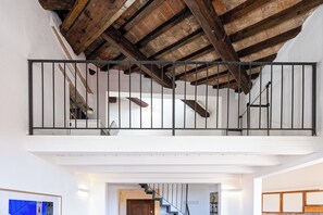 Un intérieur à plusieurs niveaux avec des poutres apparentes, un escalier et une rambarde.