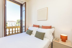 Une chambre d’hôtel avec un lit, des oreillers, une table de chevet, une lampe et une fenêtre donnant sur des immeubles.