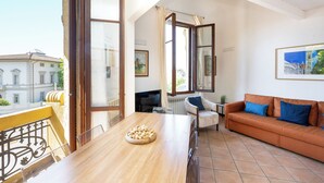 Un balcón con una mesa de madera y un cuenco de fruta, un sofá con cojines azules y un cuadro en la pared.