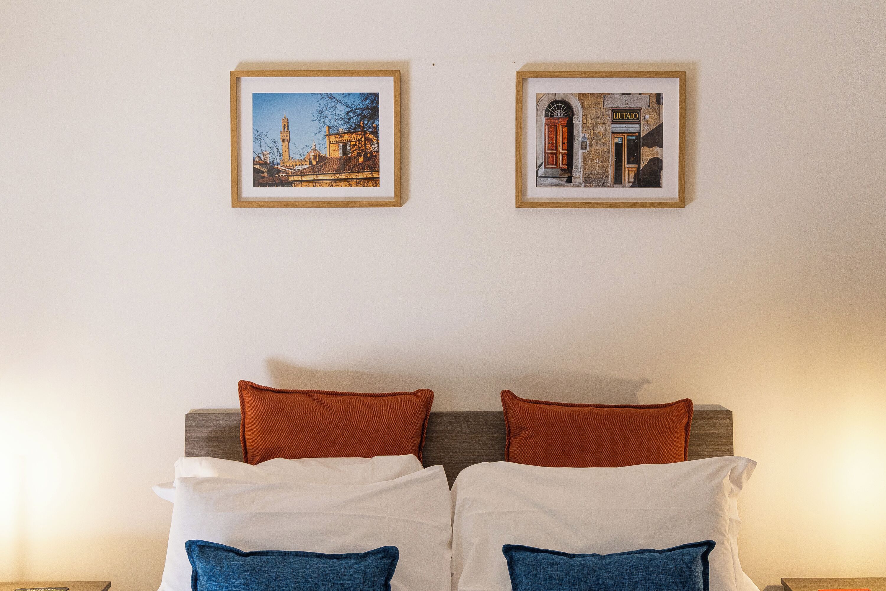 Una habitación de hotel con una cama, dos cuadros en la pared y una mesita de noche.