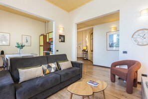A modern living room with a sofa, coffee table, and a unique chair. There is a dining area with a table and chairs, and a kitchen in the background. - Rental In Rome Rosselli Santa Maria Novella Palace (Florence)