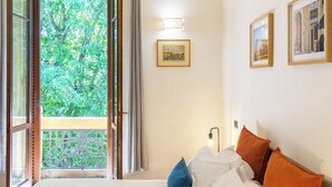 Hotellihuone, jossa on sänky, yöpöytä, seinään kiinnitetty valaisin ja kehystetyt taulut.