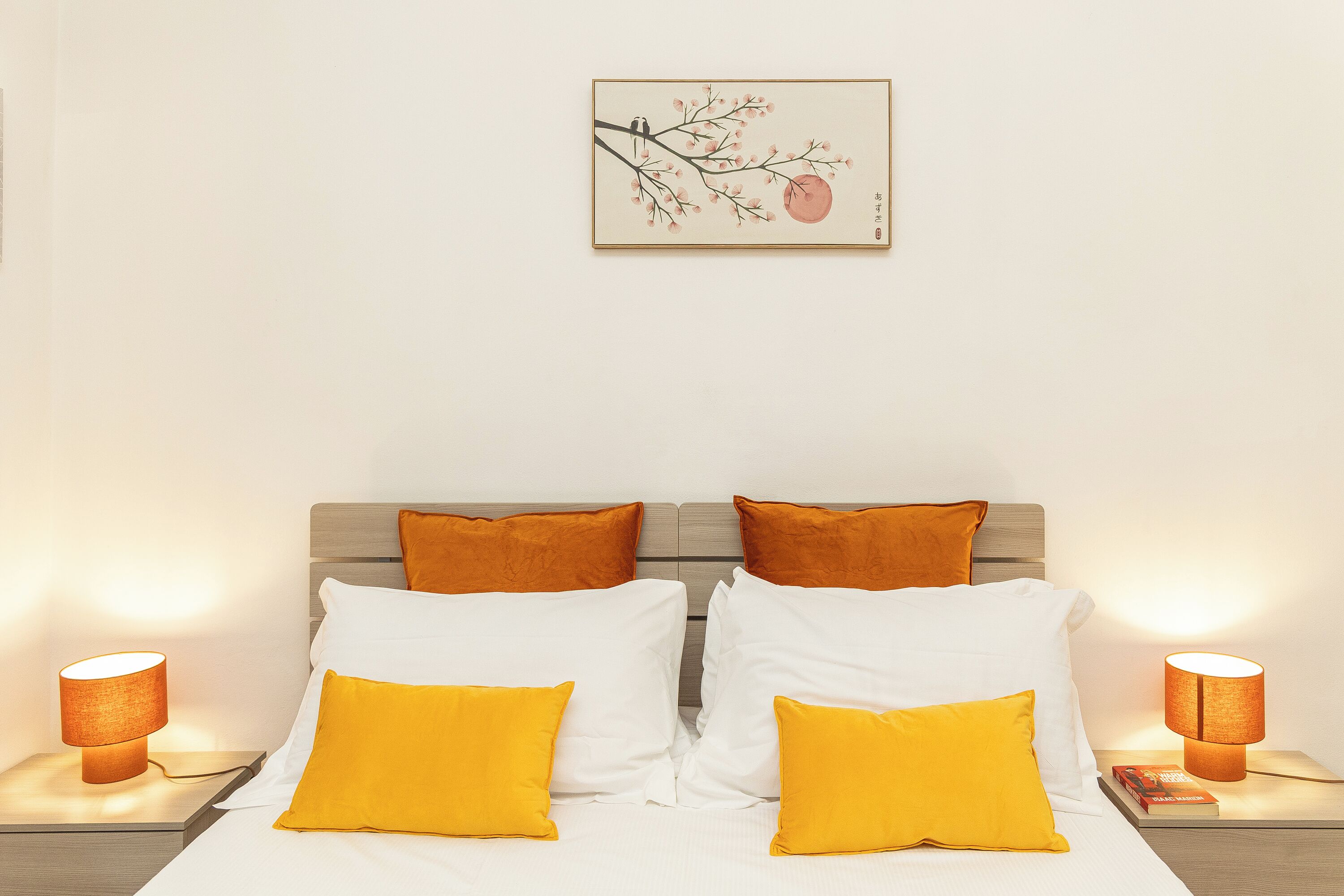 A neatly made bed with white and yellow pillows, a wooden headboard, and two bedside lamps.