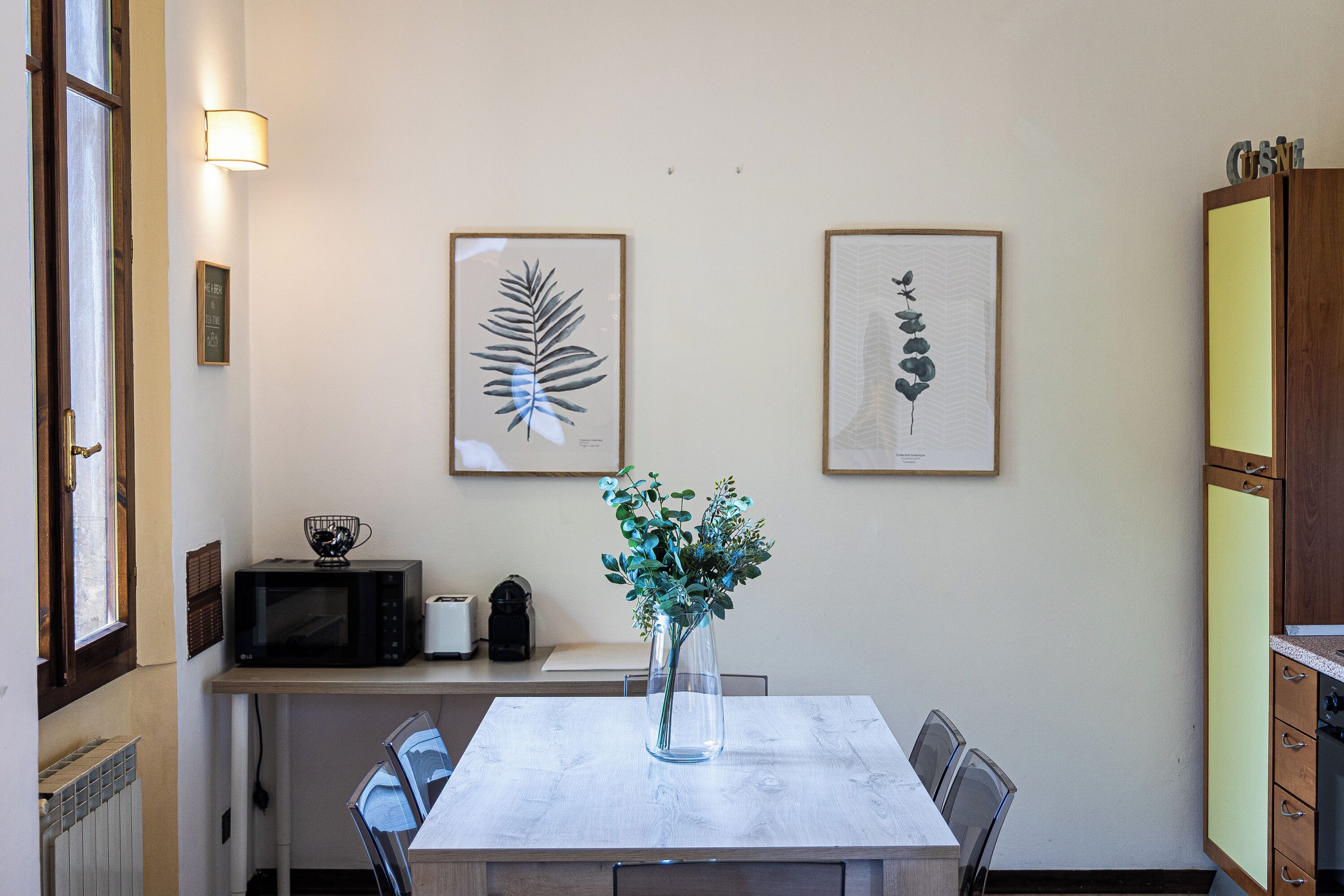 Un'area pranzo con tavolo, sedie, un vaso con fiori, un forno a microonde e stampe floreali incorniciate alle pareti.