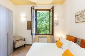 Un dormitorio con cama, una silla, una ventana con cortinas e iluminación en la pared.