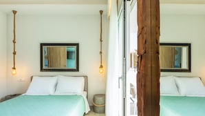 Ein Zimmer mit zwei Betten, jedes mit weißer Bettwäsche und einer türkisblauen Tagesdecke. Über den Betten befinden sich zwei an der Wand montierte Spiegel, und ein kleiner runder Tisch mit Ropesockel ist zu sehen.