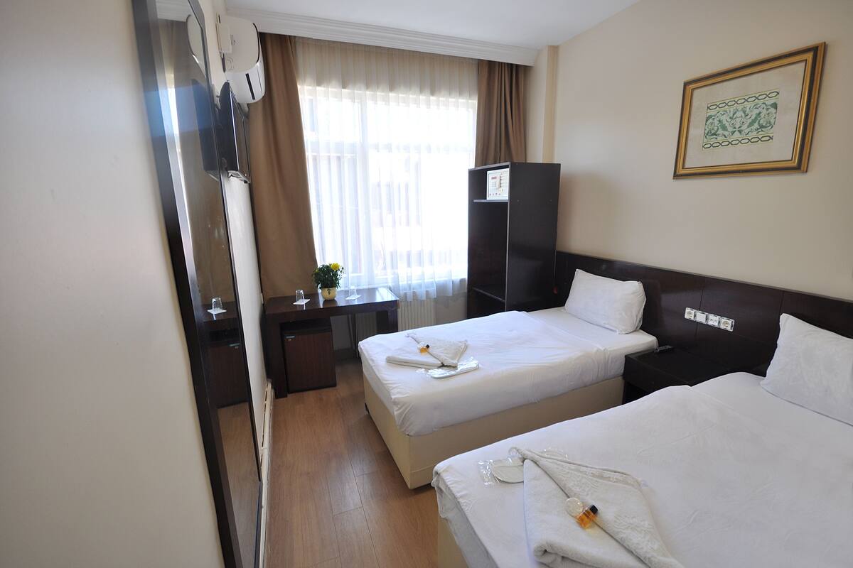 A hotel room with two beds, a desk, a wardrobe, and a window with curtains.
